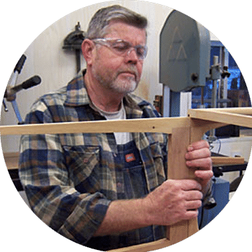 A skilled craftsman wearing safety glasses works on assembling a wooden frame in a workshop